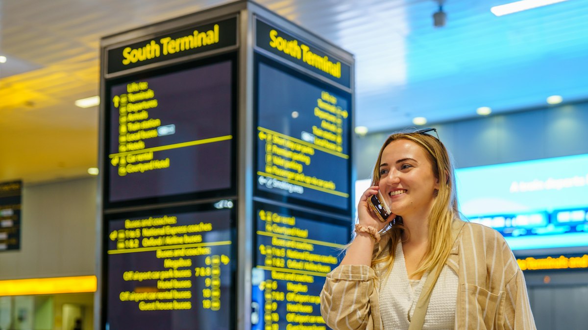 Woman on a phone call by an airport departure board